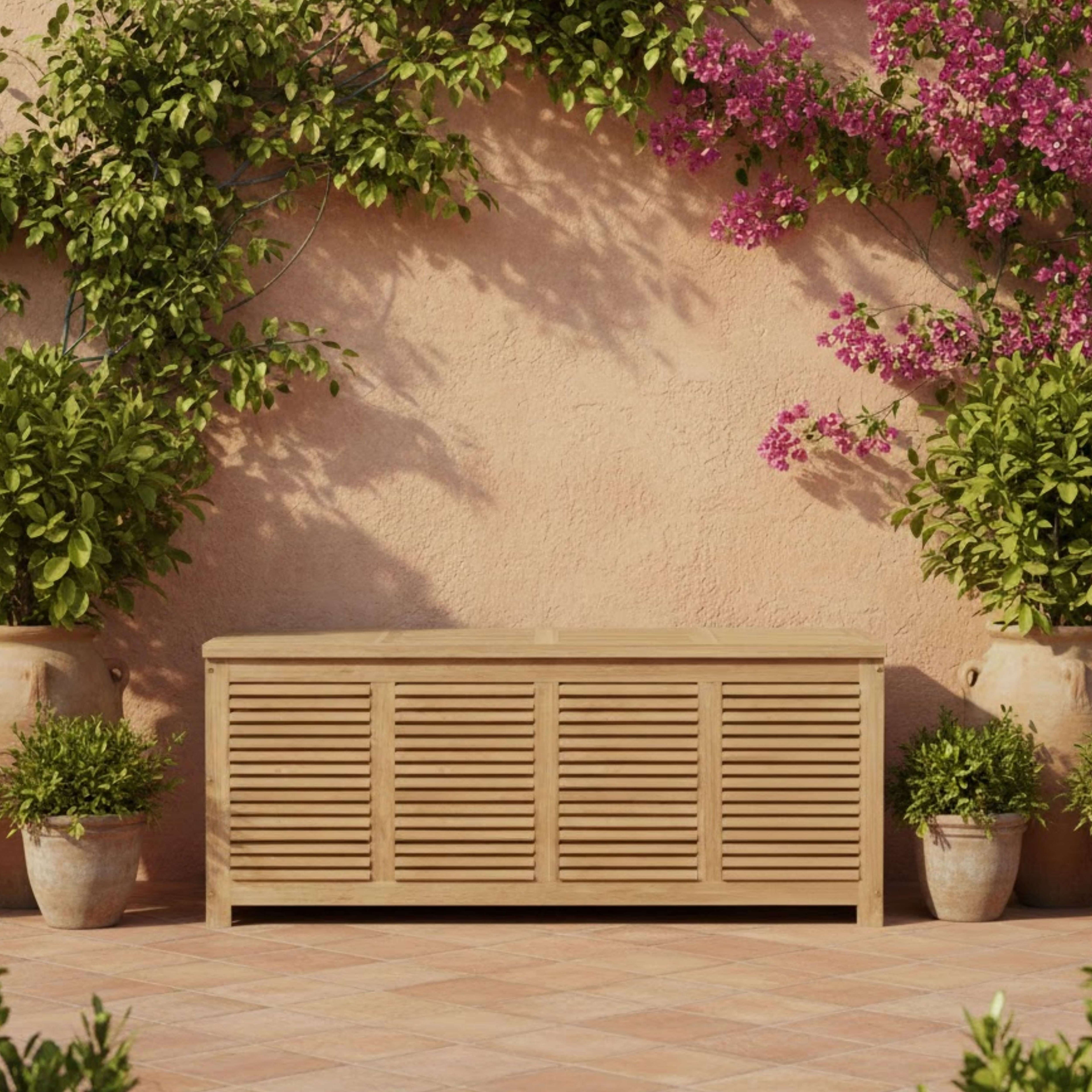 Amberly teak storage box with closed lid against a garden wall with flowering vines
