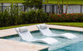 Two White Signature Chaises with headrest pillows on a shallow pool ledge; lifestyle styling example.