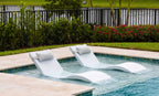 Two White Signature Chaises with headrest pillows on a shallow pool ledge; lifestyle styling example.