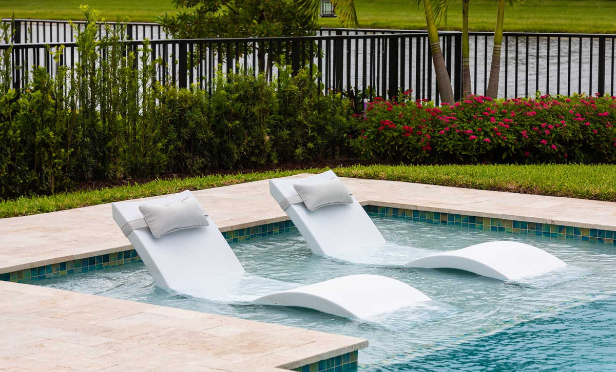 Two White Signature Chaises with headrest pillows on a shallow pool ledge; lifestyle styling example.