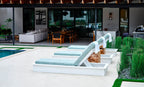 Side view of white-frame Ledge Lounger Echo chaises with blue-gray cushions and towels beside a pool.