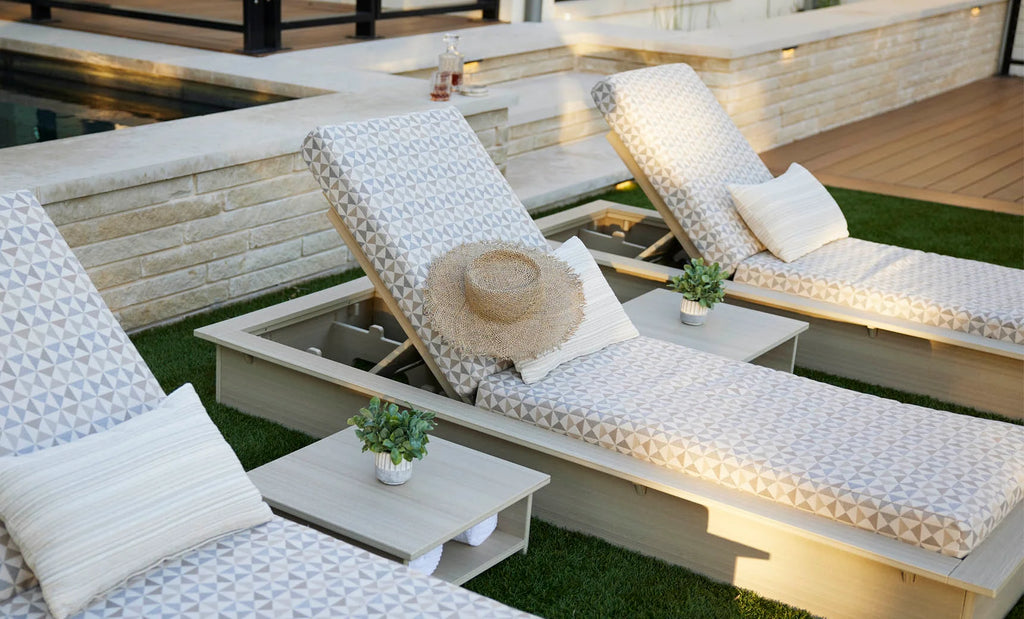 Ledge Lounger Echo chaises with pale woodgrain-look frames, geometric-pattern cushions and square side tables beside a pool.