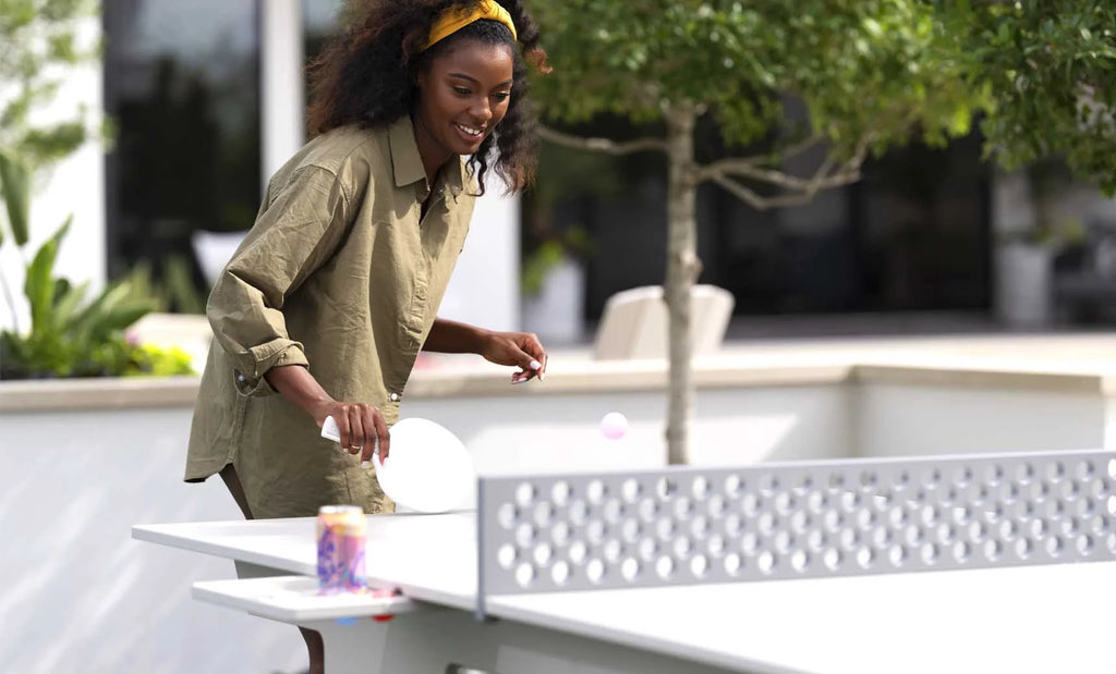 Woman playing outdoors on the all-weather table tennis set with the pull-out accessory tray beside the table