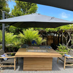Louvre fire pit dining table with a lit glass-enclosed burner and woven seating on a garden patio.