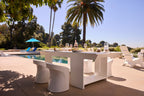 Ledge Lounger Table Tennis Set arranged poolside, surrounded by palm trees, lounge chairs, and a sun umbrella