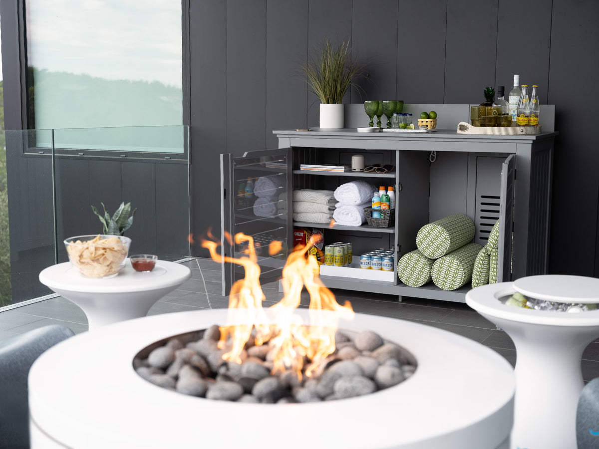 Lit Halo firepit in front of an open gray outdoor credenza with towels and serving accessories