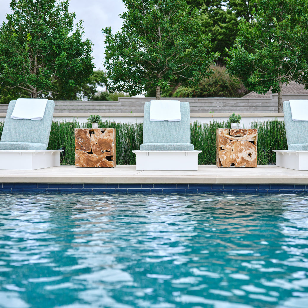 White Ledge Lounger Echo Chaises with blue-gray cushions arranged beside a pool with wood side tables.