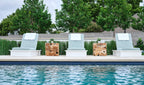 Front view of three white-frame Ledge Lounger Echo chaises with blue-gray cushions and wood side tables beside a pool.