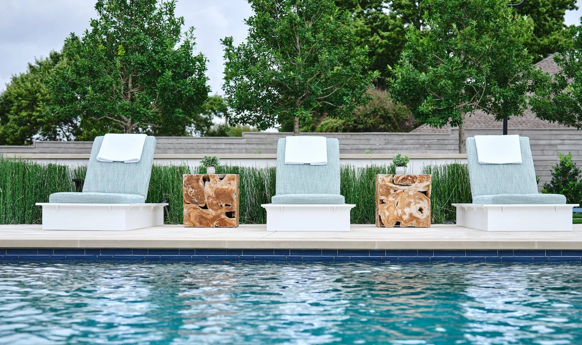 Front view of three white-frame Ledge Lounger Echo chaises with blue-gray cushions and wood side tables beside a pool.