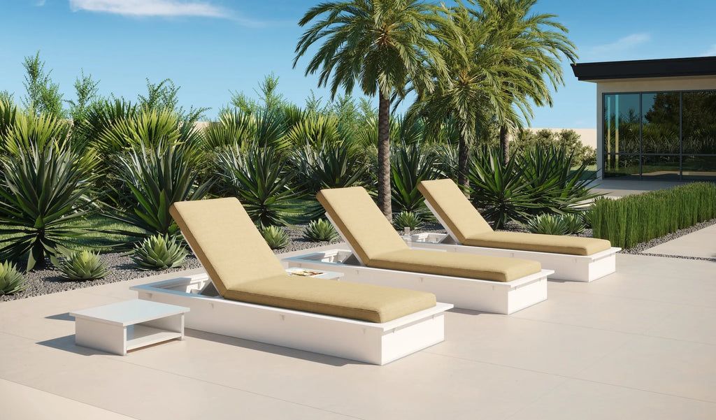 White adjustable poolside chaise lounges with beige cushions and a matching side table on a palm-lined patio.
