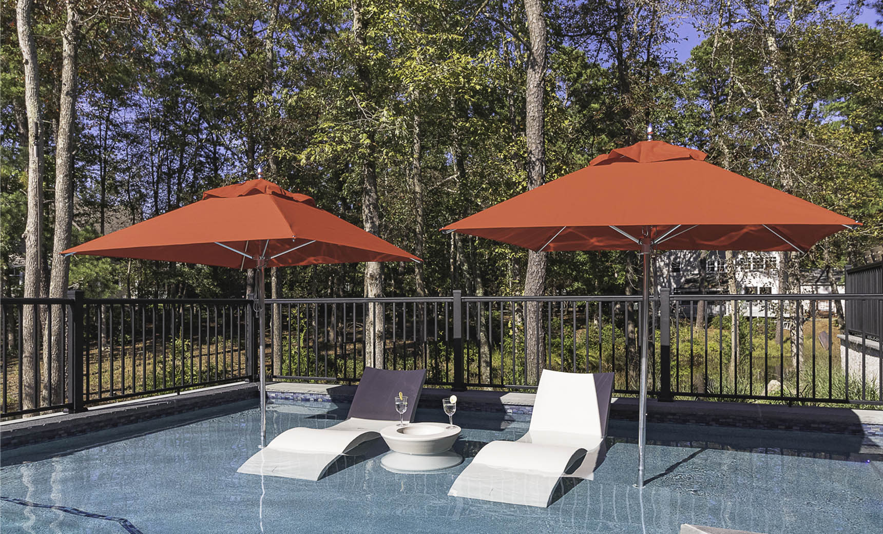 Two red 9-foot Premier Umbrellas shading in-pool chaise lounges on a residential pool ledge