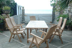 Bahama Katana teak extension dining table and six reclining armchairs on a seaside stone patio, with a white picket gate and the ocean behind