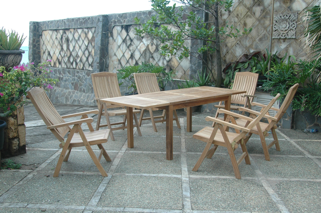 Bahama Katana teak extension table with six reclining armchairs on a stone patio beside a stone garden wall with lattice panels and tropical plants