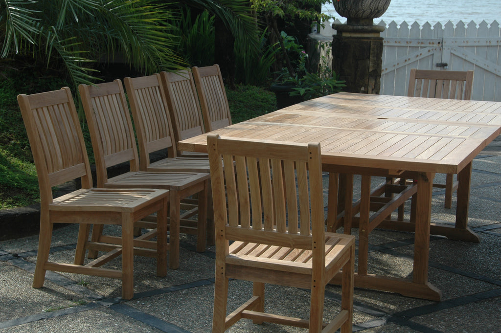 Close view of the Sahara Rialto extension table's slatted teak top, umbrella hole and trestle base with armless Rialto chairs alongside on a stone patio