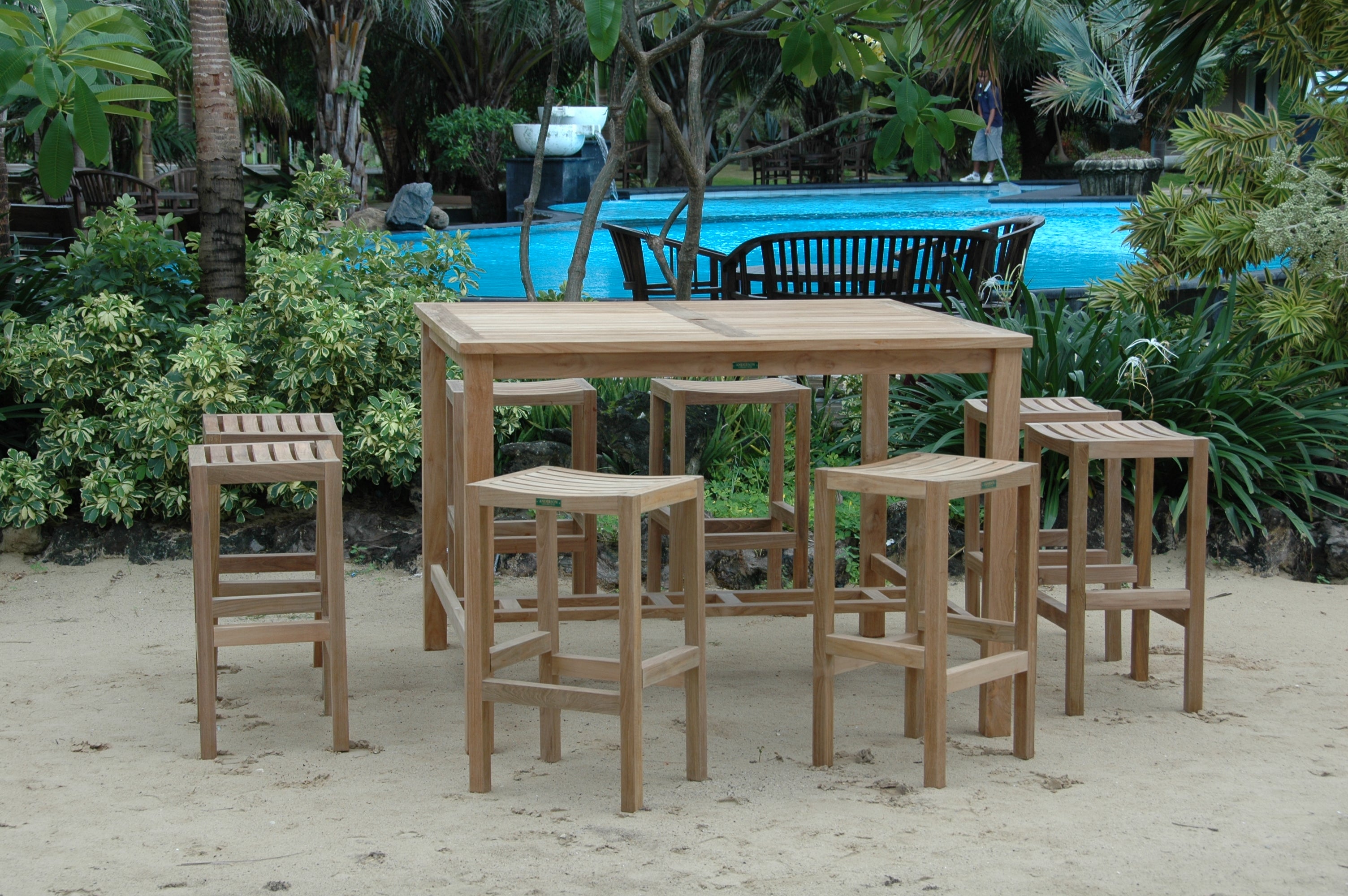 Windsor 59-inch square teak bar table with eight Montego backless bar chairs beside a resort pool