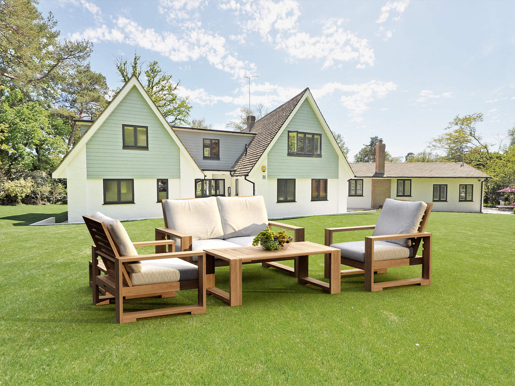 Teak loveseat conversation set with two armchairs and tables arranged on a lawn outside a house.