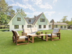 Teak loveseat conversation set with two armchairs and tables arranged on a lawn outside a house.