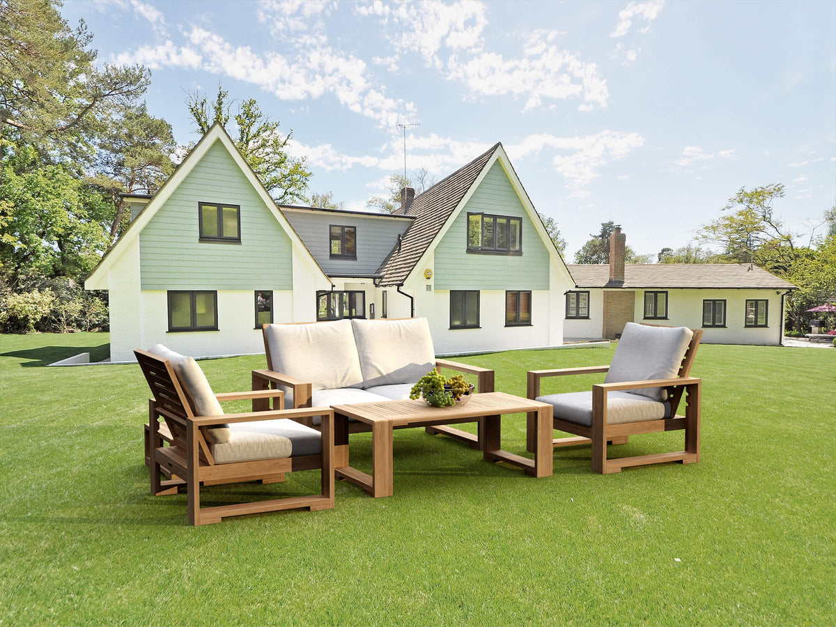 Teak loveseat conversation set with two armchairs and tables arranged on a lawn outside a house.
