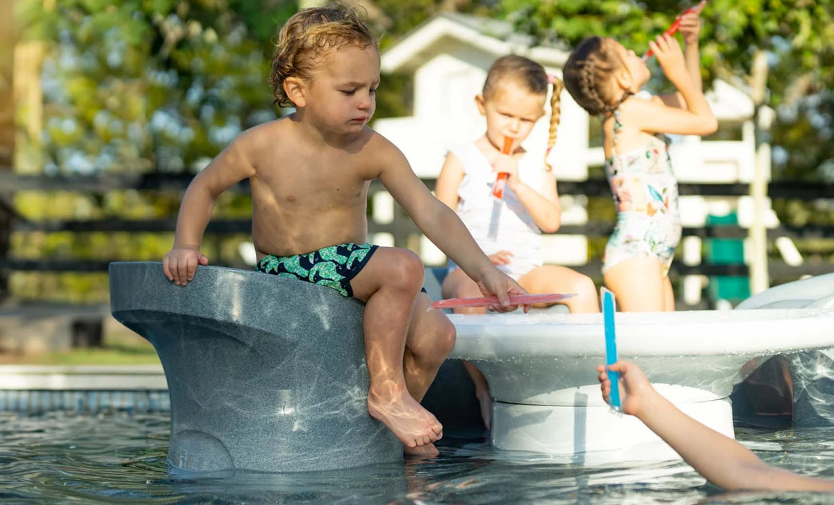 Children seated on sculptural swim-up pool barstools beside a pool counter.