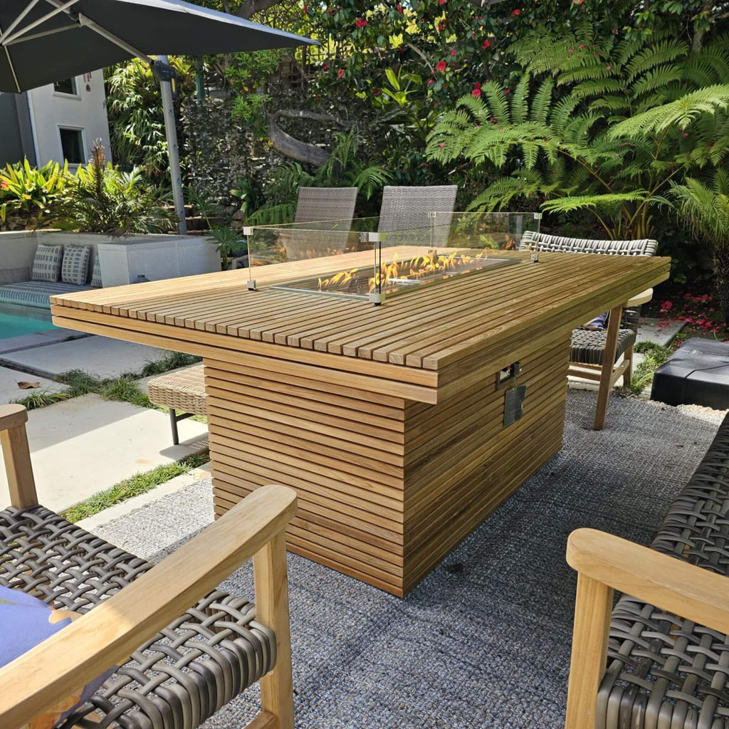 Close poolside view of the Louvre slatted teak tabletop, lit burner, glass wind guard and base controls.