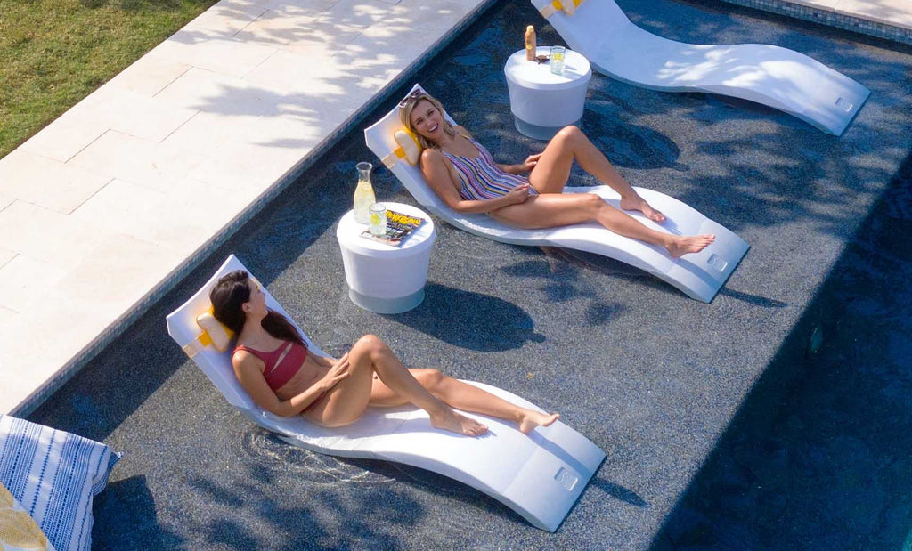 Two White Signature Chaises with headrest pillows and side tables on a shallow pool ledge