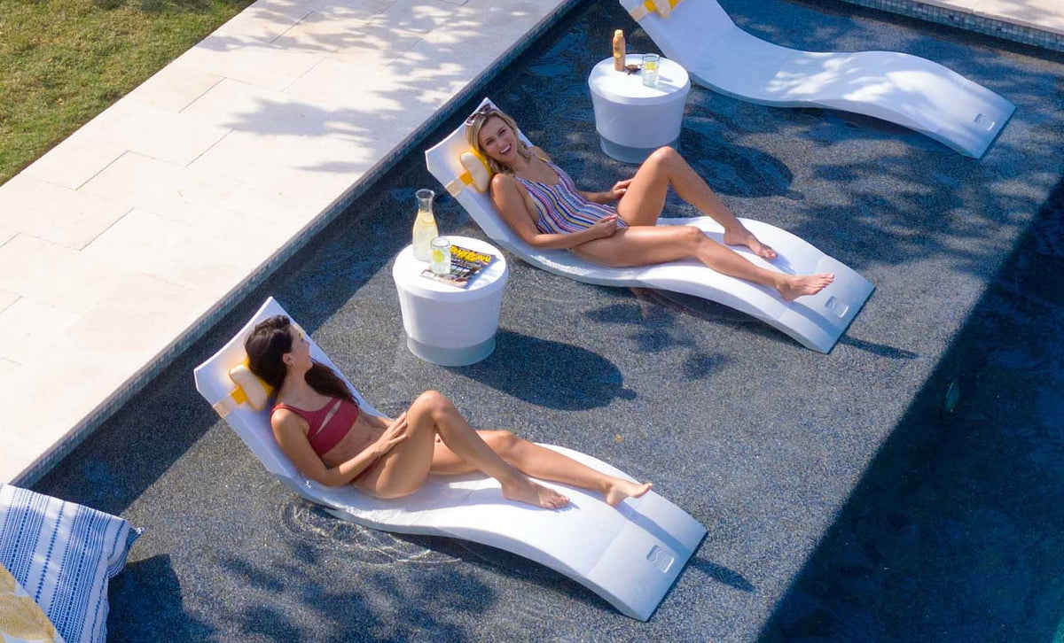 Two White Signature Chaises with headrest pillows and side tables on a shallow pool ledge