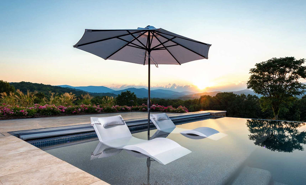 White Signature Chaises beneath an umbrella on a shallow pool ledge at sunset