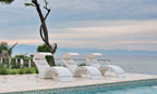 Three White Signature Chaise Deep loungers with shades and pillows on an ocean-view pool ledge