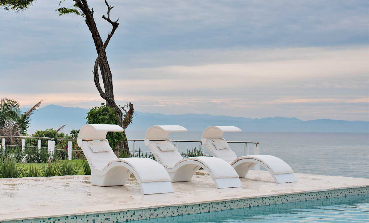Three White Signature Chaise Deep loungers with shades and pillows on an ocean-view pool ledge