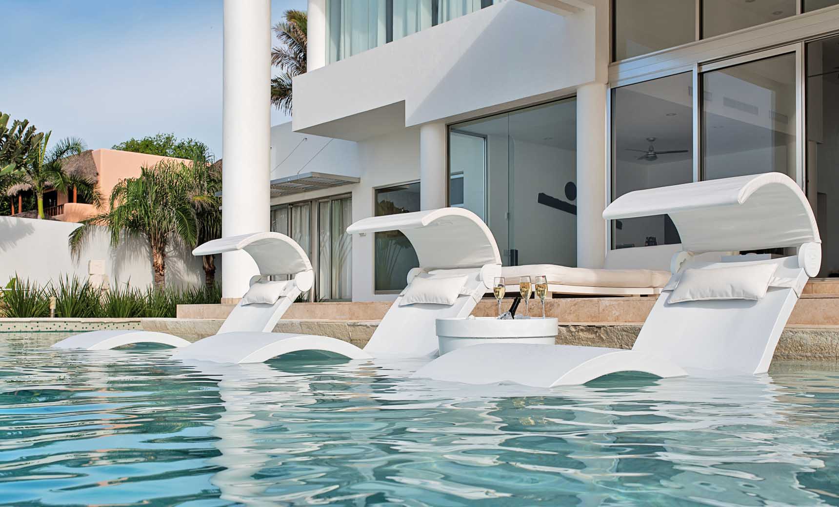 Three White Signature Chaise Deep loungers with shades and pillows in an infinity pool