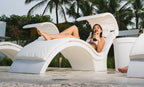 Person reclining on a White Signature Chaise Deep with shade and pillow beside a pool