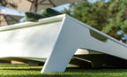 White Cornhole Toss board with integrated carry handle on grass