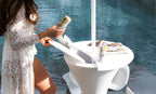Guest opening the ice-bin lid on a white in-pool umbrella stand beside the water.