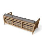 Rear view of a teak outdoor sofa with gray cushions and a slatted back.