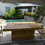 Poolside view of the Louvre teak fire table, showing the lit glass wind guard and controls on the base.