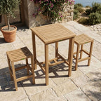 Avalon teak bar-height table with two backless chairs on a stone patio