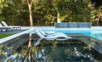 White Signature Chaises and side tables reflected beside a modern pool