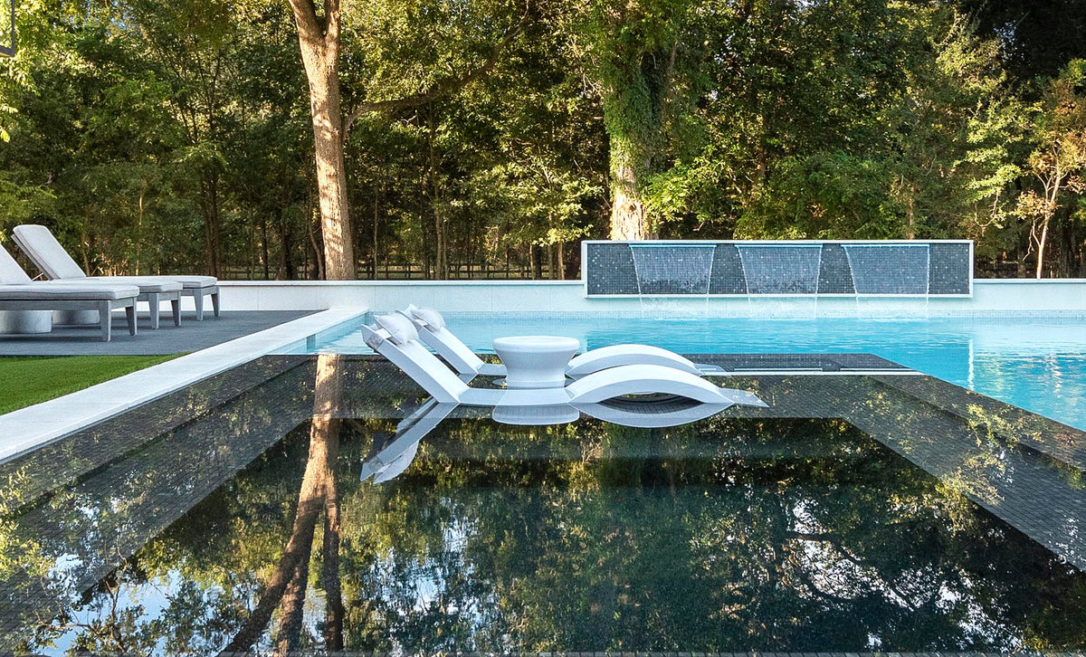 White Signature Chaises and side tables reflected beside a modern pool