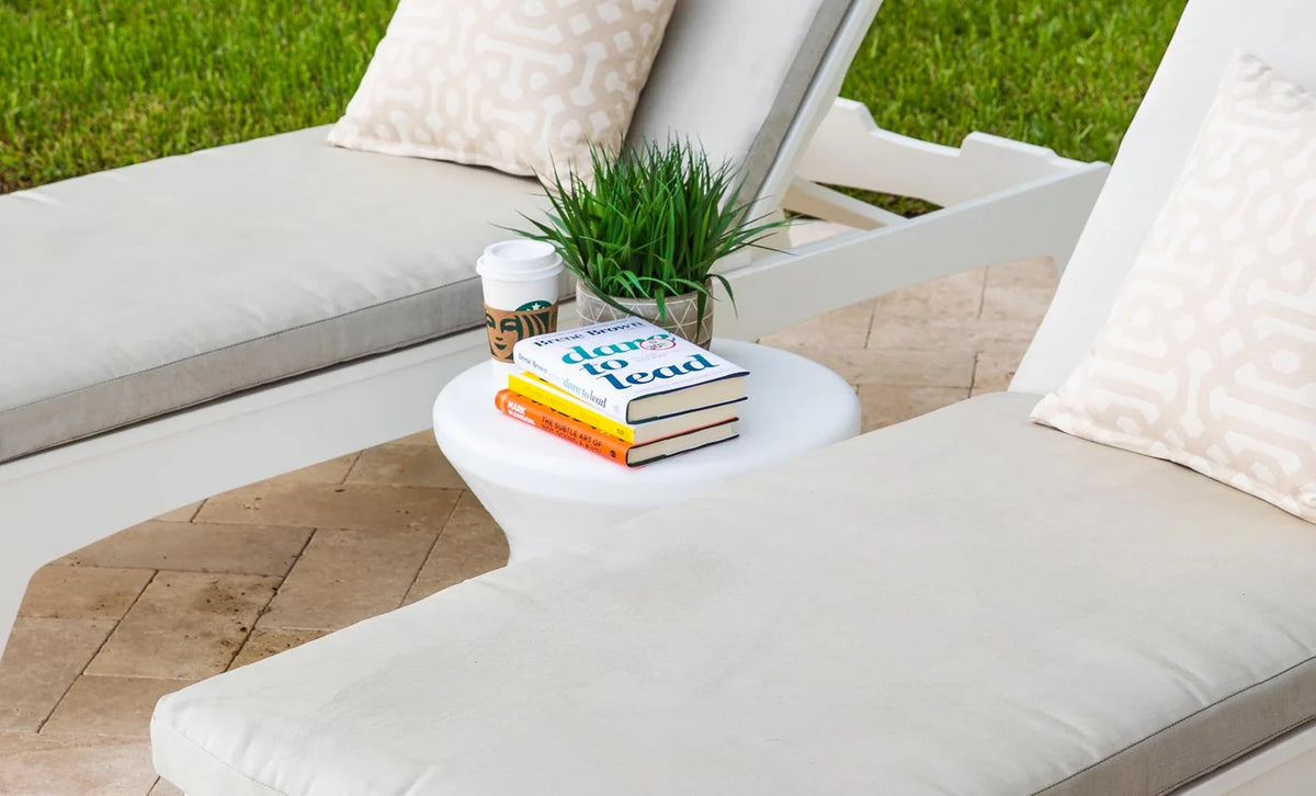 White Signature Side Table holding books and a drink between cushioned patio loungers; styling accessories and loungers not included